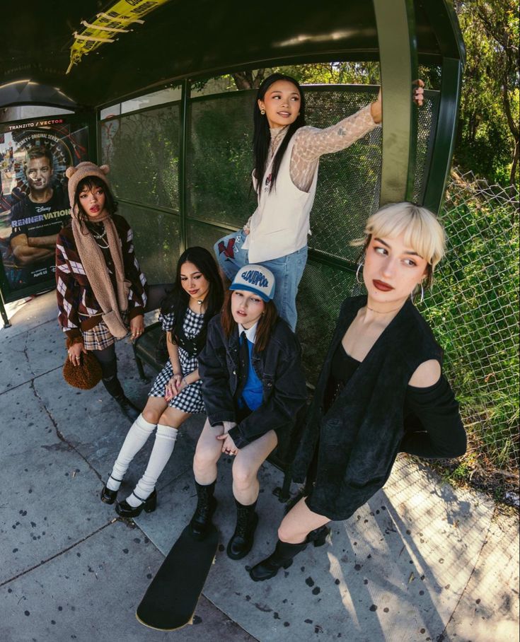 four young women posing for a photo in front of a bus stop with their skateboards