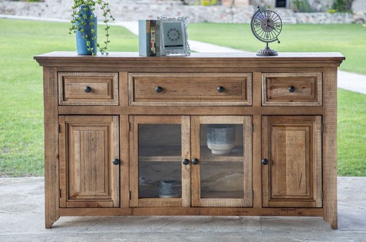 a wooden sideboard with glass doors and drawers on the top, in front of a lawn