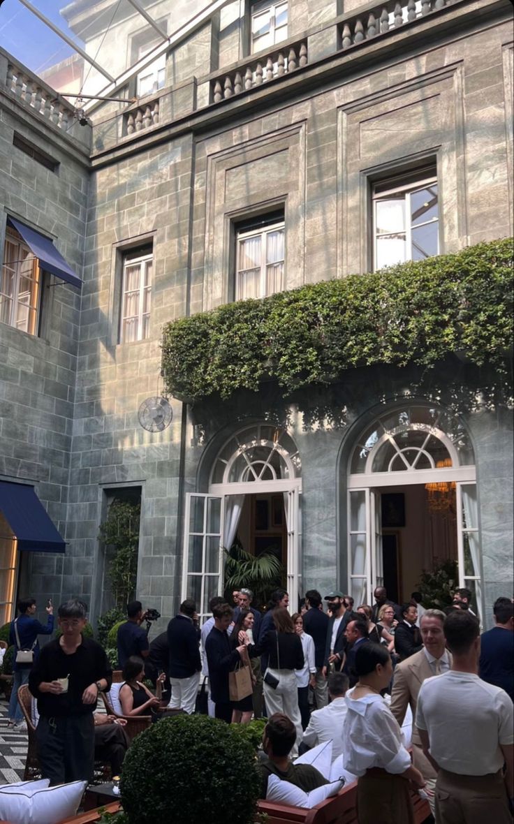 a group of people standing in front of a building with lots of windows and doors