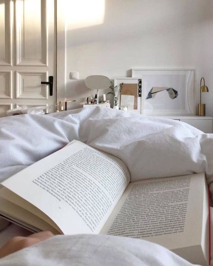 an open book sitting on top of a bed in a room with white sheets and pillows