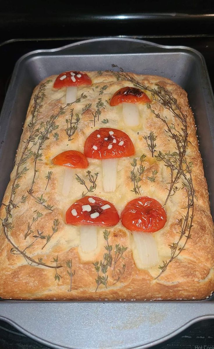 a square pizza with tomatoes, cheese and herbs on it in a baking pan that is ready to go into the oven