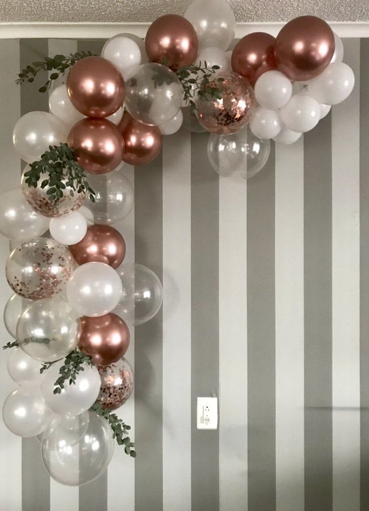 some balloons and greenery are hanging from the wall in front of a striped wall