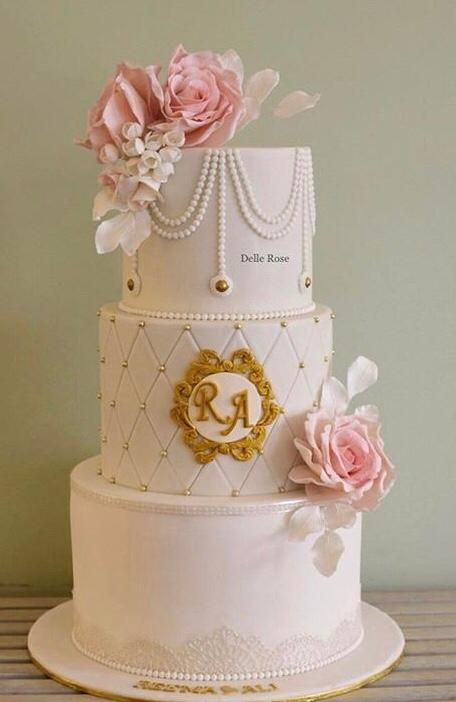 a three tiered white cake with pink flowers on top and gold trimmings