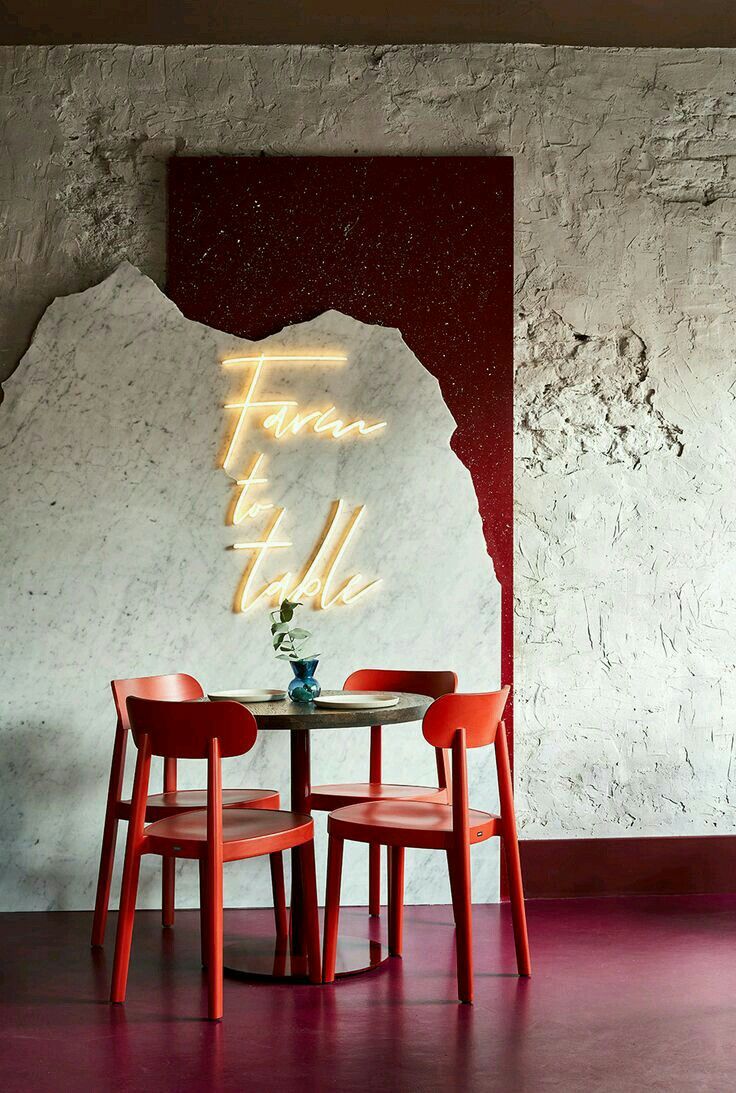 two red chairs sitting at a table with a neon sign on the wall behind it