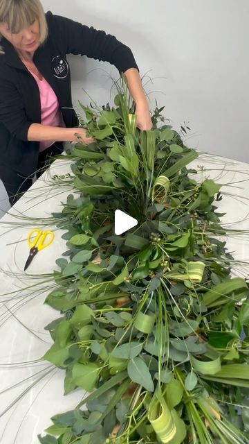 a woman is making a wreath out of fake greenery on a table with scissors