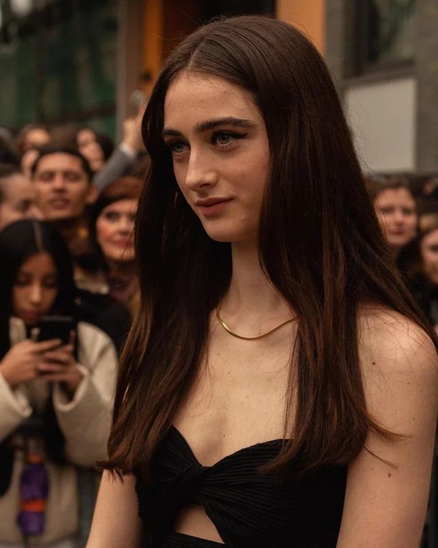 a woman with long brown hair standing in front of a group of people holding cell phones