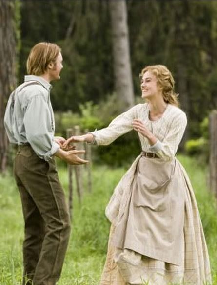 a man and woman dressed in period clothing dancing together outside with trees in the background