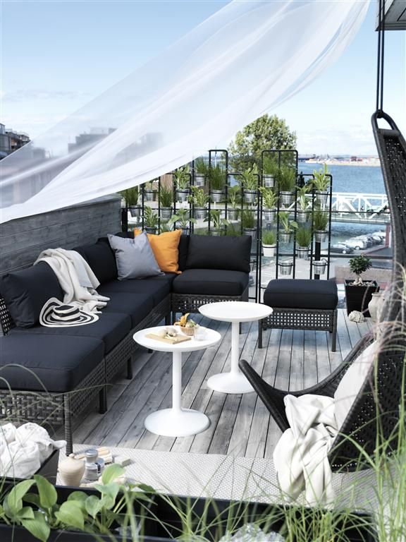 an outdoor living area with black furniture and white curtains on the balcony overlooking the water