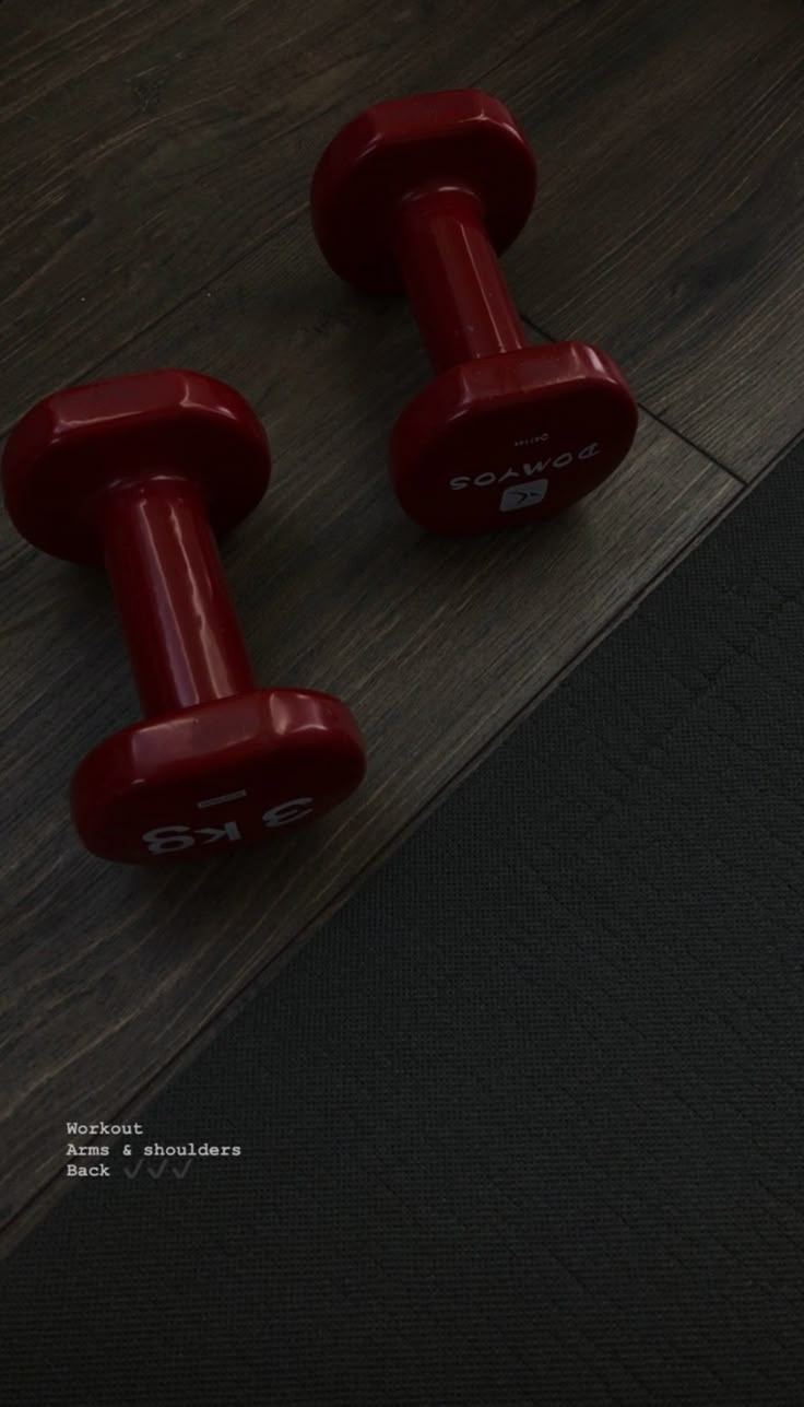 two red dumbbells sitting on top of a wooden floor next to each other