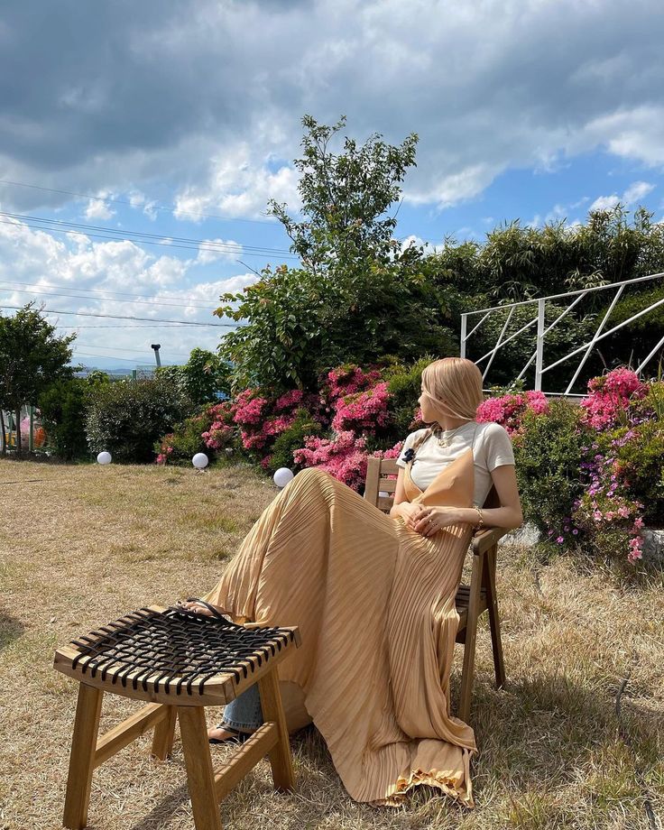 a woman sitting on top of a wooden bench next to a flower filled park area