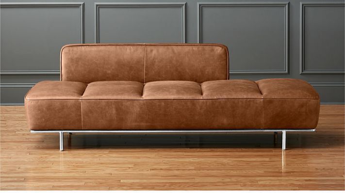 a brown couch sitting on top of a hard wood floor next to a gray wall