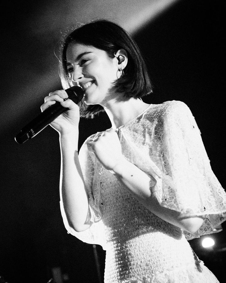 a woman singing into a microphone while wearing a white dress and standing in front of a stage