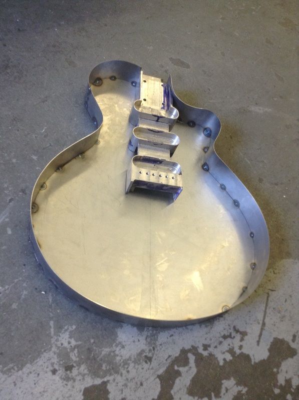 an electric guitar sitting on top of a cement floor next to a metal object with four strings attached