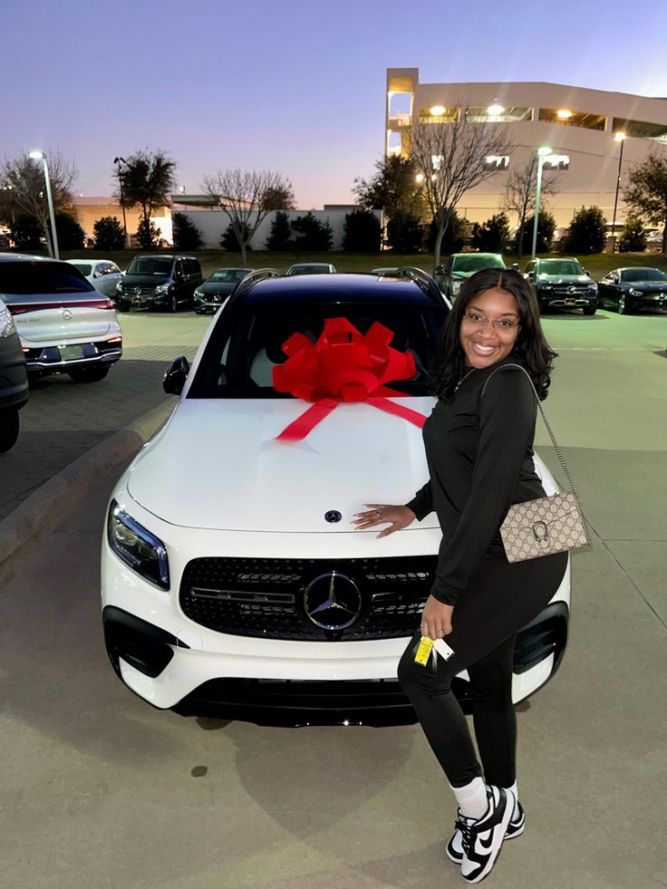 a woman standing in front of a white car with a red bow on the hood