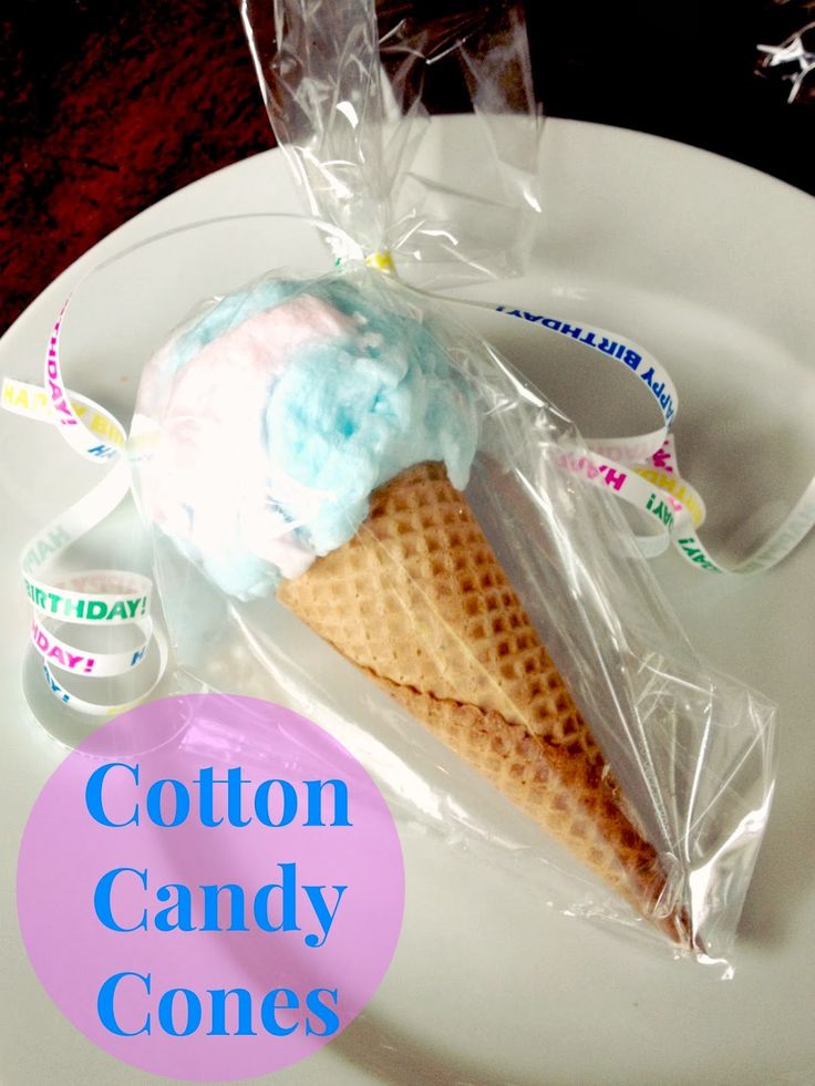 cotton candy cones on a white plate with plastic wrapper around the cone and some candies