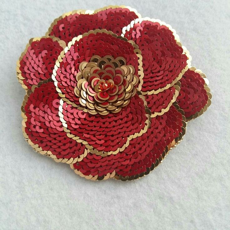 a red and gold flower brooch sitting on top of a white surface