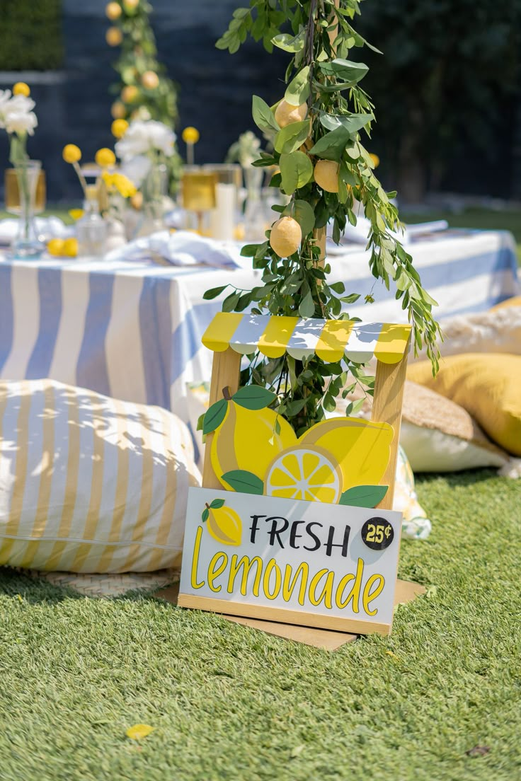 a lemonade sign sitting on top of a grass covered field next to a table