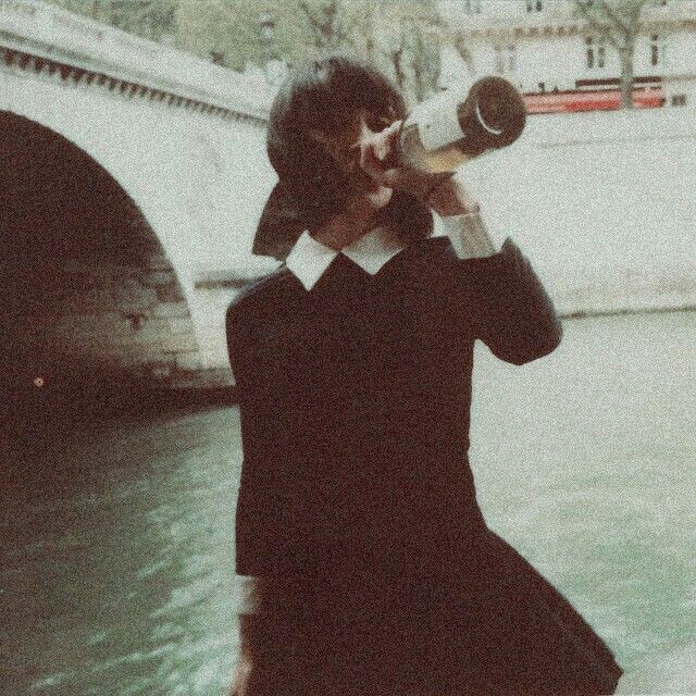 a woman in black dress holding up a camera to her face while standing next to a river