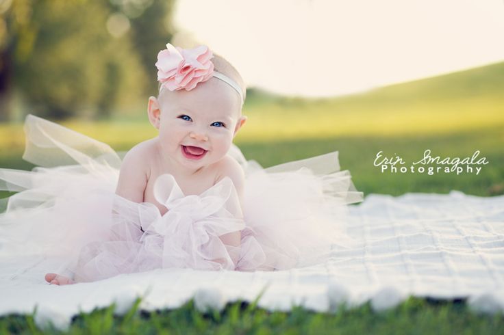 a baby girl wearing a pink tutu on top of a blanket in the grass