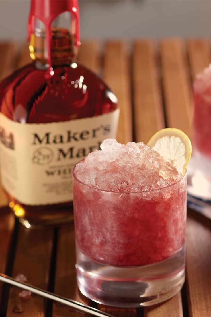 a bottle of maker's mark next to a glass filled with ice and a lemon slice