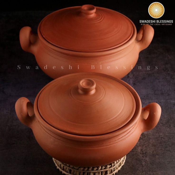 two clay pots sitting next to each other on top of a wicker basket in front of a black background