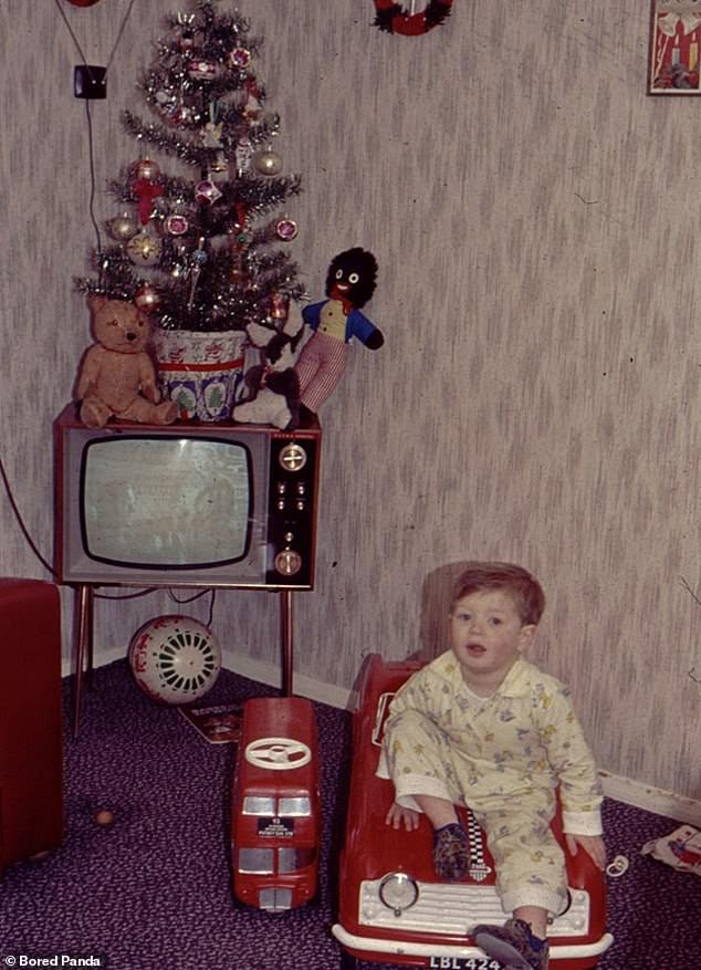 a young boy sitting in a toy car next to a christmas tree and television set