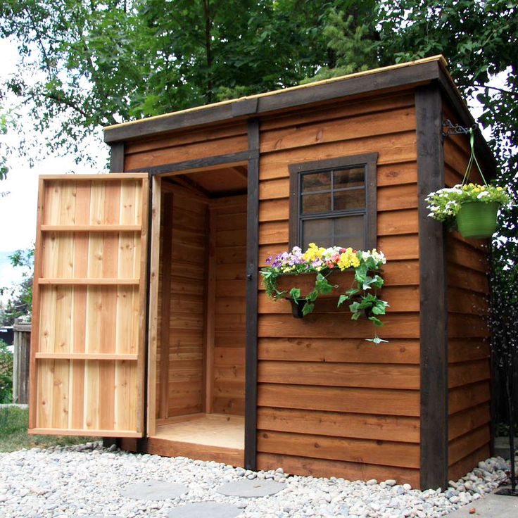 a wooden shed with its door open and flowers growing in the window box on the side