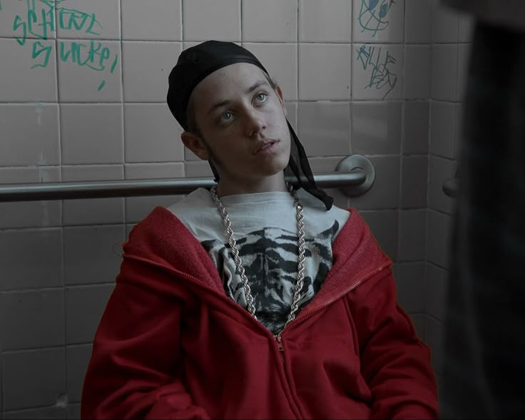 a young man with dreadlocks sitting in a bathroom stall