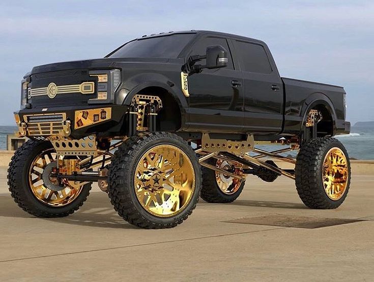 a black truck with gold wheels parked on the beach