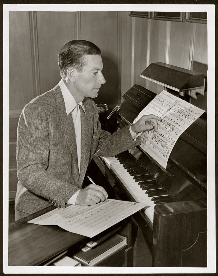 a man in a suit sitting at a piano and playing the organ with sheet music