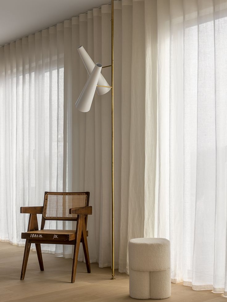 a wooden chair sitting next to a tall lamp in a room with white drapes on the windows