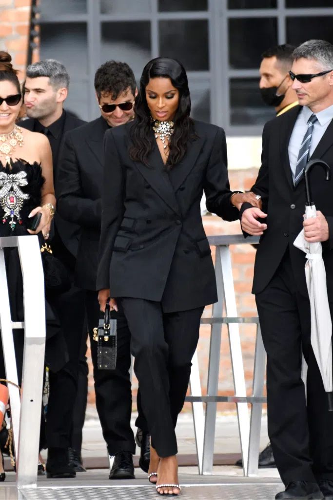 a woman in a black suit and tie walking down the street with other people behind her