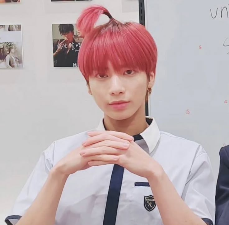 a man with red hair and suspenders sitting in front of a whiteboard holding his hands to his chest