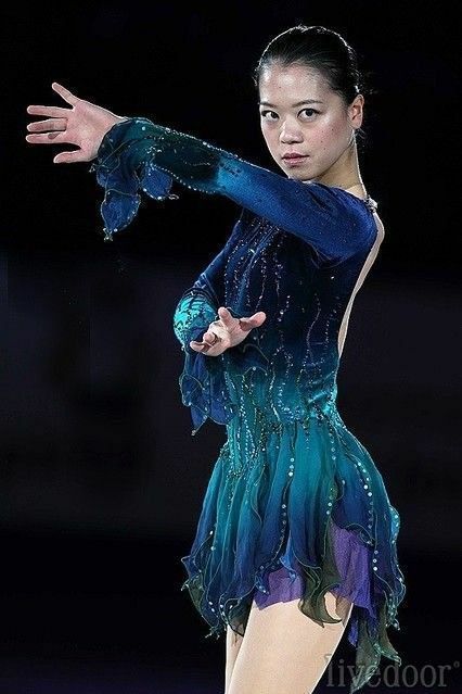 a woman in a blue and green dress is doing a trick on a skateboard