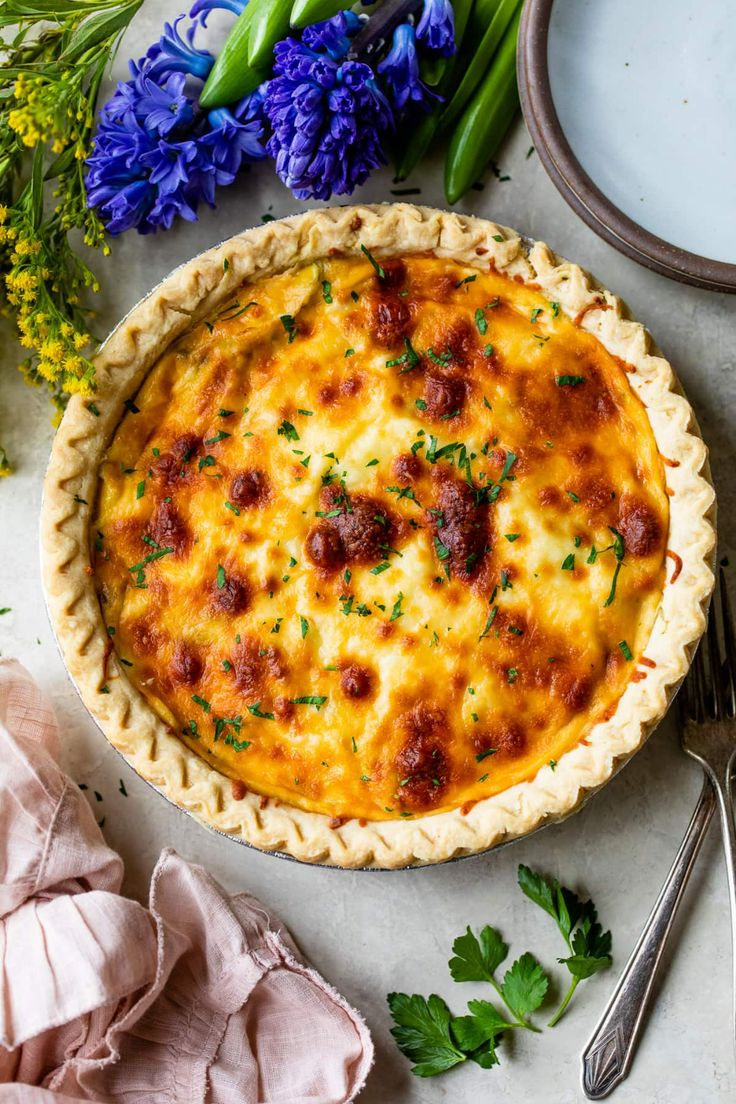 a quiche with meat and cheese in a pie pan on a table next to flowers