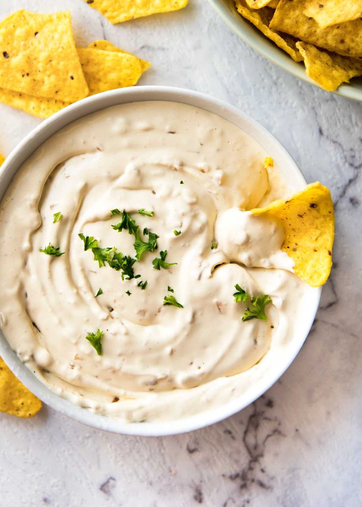 a white bowl filled with dip surrounded by tortilla chips