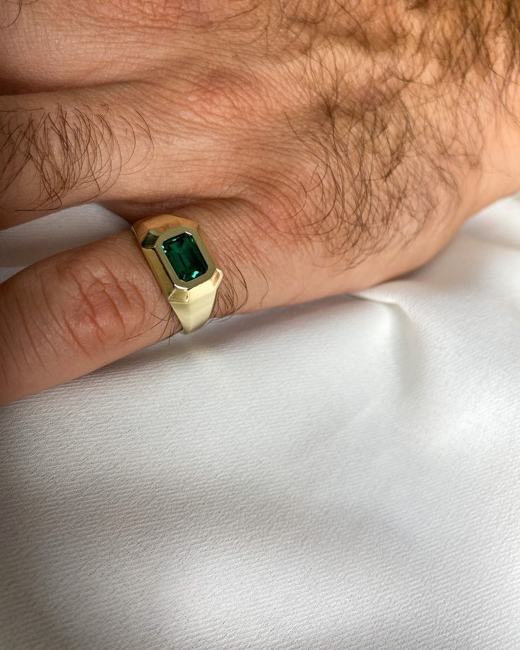 a man's hand with a ring on it and a green stone in the middle