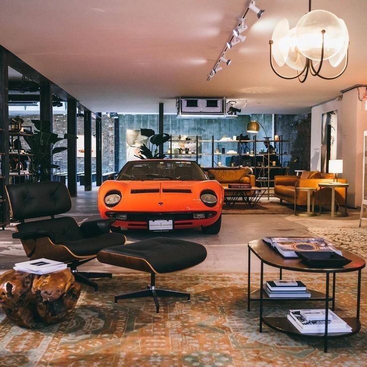 an orange sports car is parked in the living room next to a coffee table and chairs