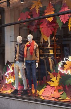 two mannequins in front of a store window with autumn leaves on display