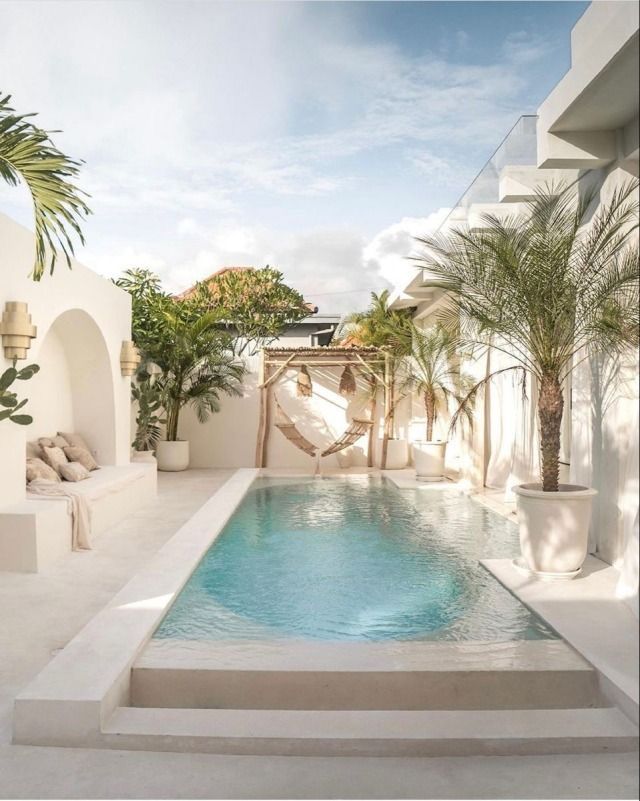 an outdoor swimming pool surrounded by white walls and palm trees, with a hammock in the middle