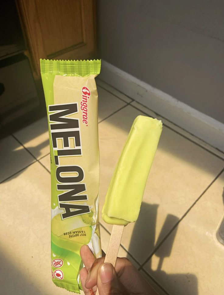 a hand holding a yellow and green ice cream bar on a toothbrush in front of a tiled floor