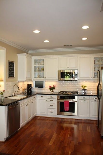 a kitchen with white cabinets and stainless steel appliances, wood flooring and hardwood floors