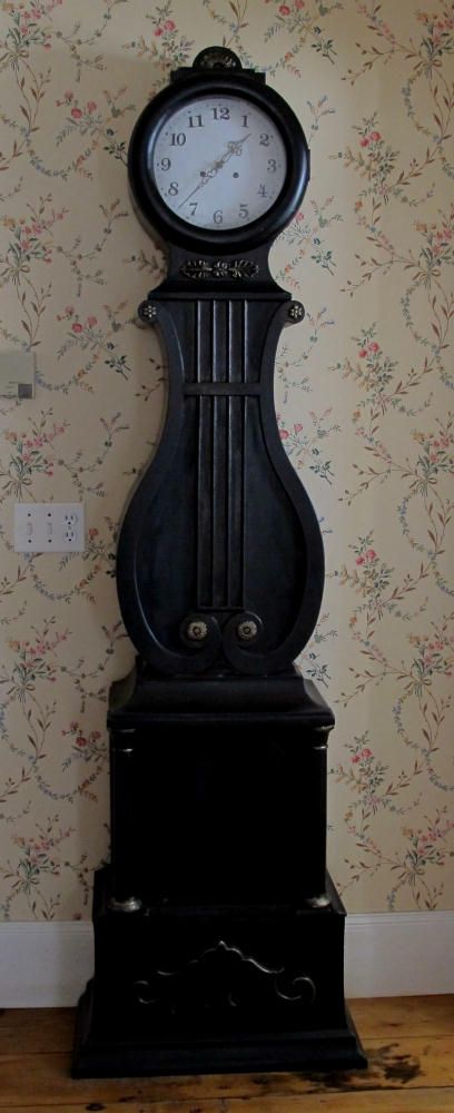 an old black clock sitting on top of a wooden table next to a wallpapered wall