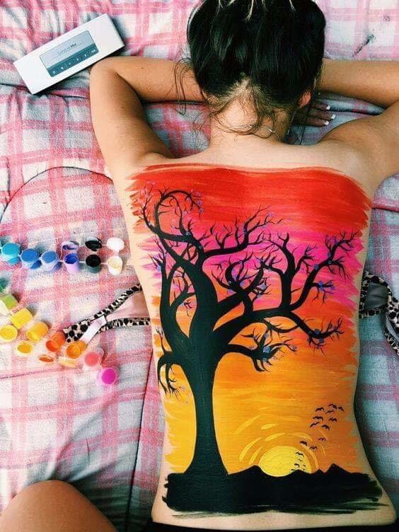 a woman laying in bed with her back to the camera and painting on her body