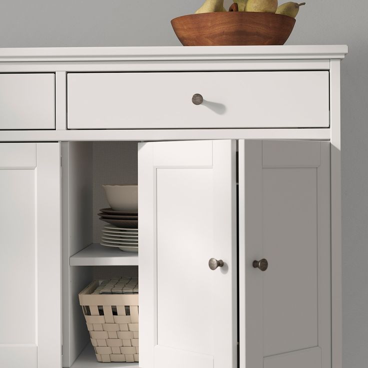 a white cabinet with two doors open and plates in the bottom drawer on top of it