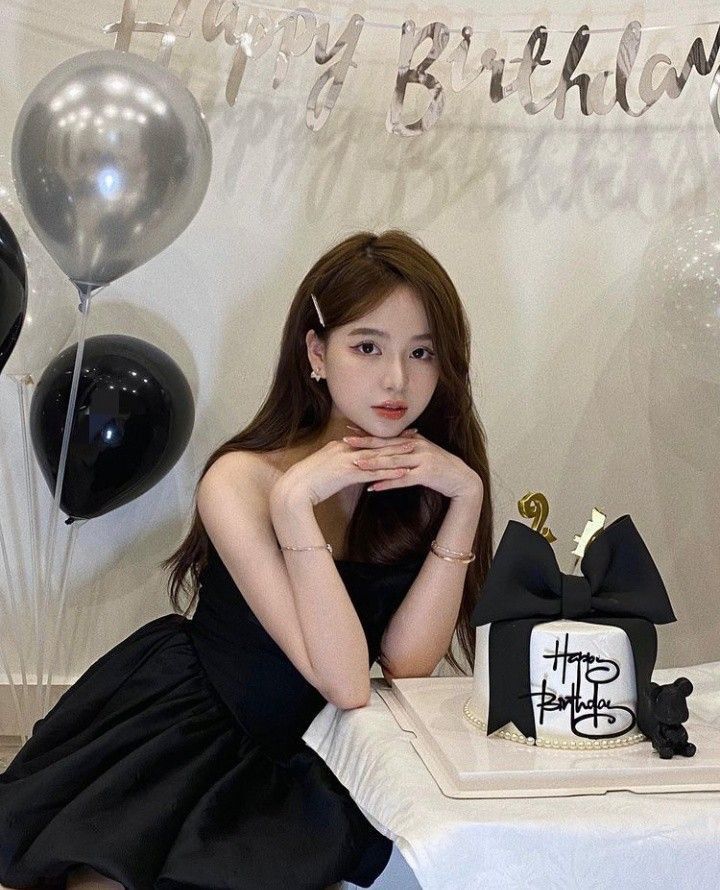 a woman sitting on a table with balloons and a cake