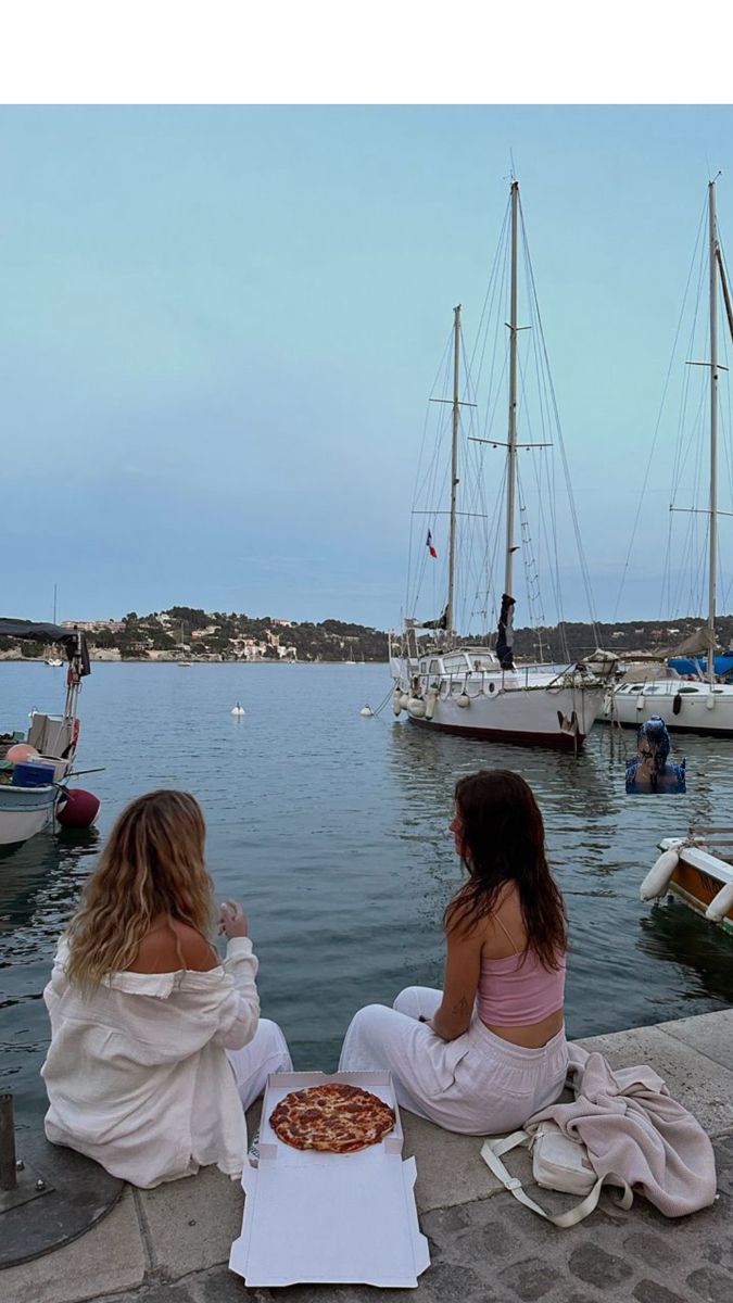 two women sitting on the dock eating pizza