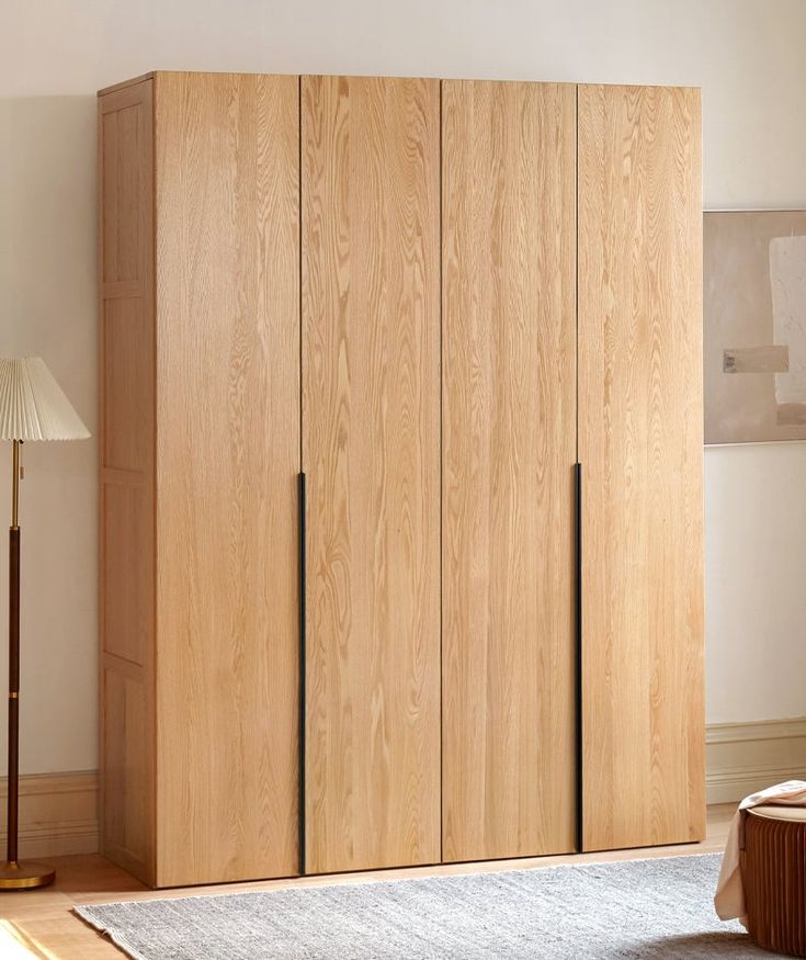 a bedroom with a bed and wooden cabinets next to a lamp on the floor in front of a white wall