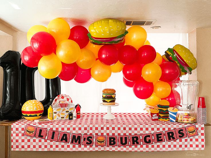 a table topped with lots of balloons and hamburgers on it's sides next to a wall