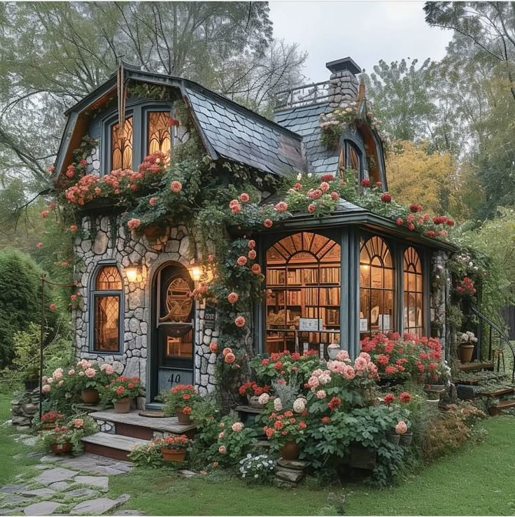 a small house with lots of flowers growing on the front and side windows, surrounded by greenery